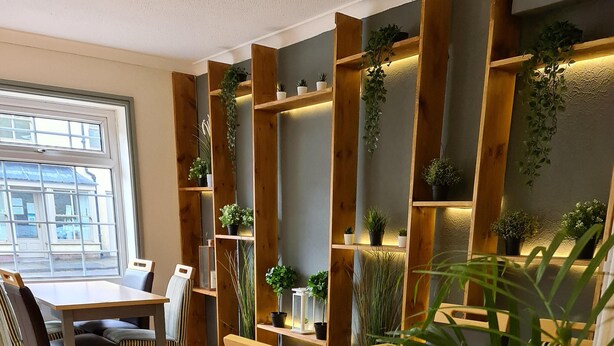 A dining area with wooden furniture, potted plants, and a large window.