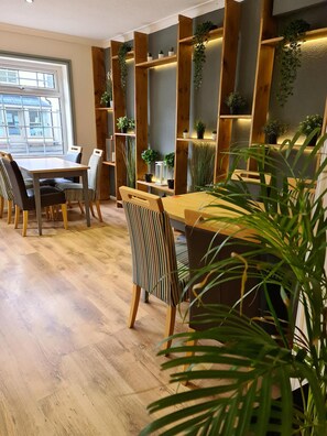 A dining area with wooden furniture, potted plants, and a large window. - The Lamb and Flag Inn (Rhayader)