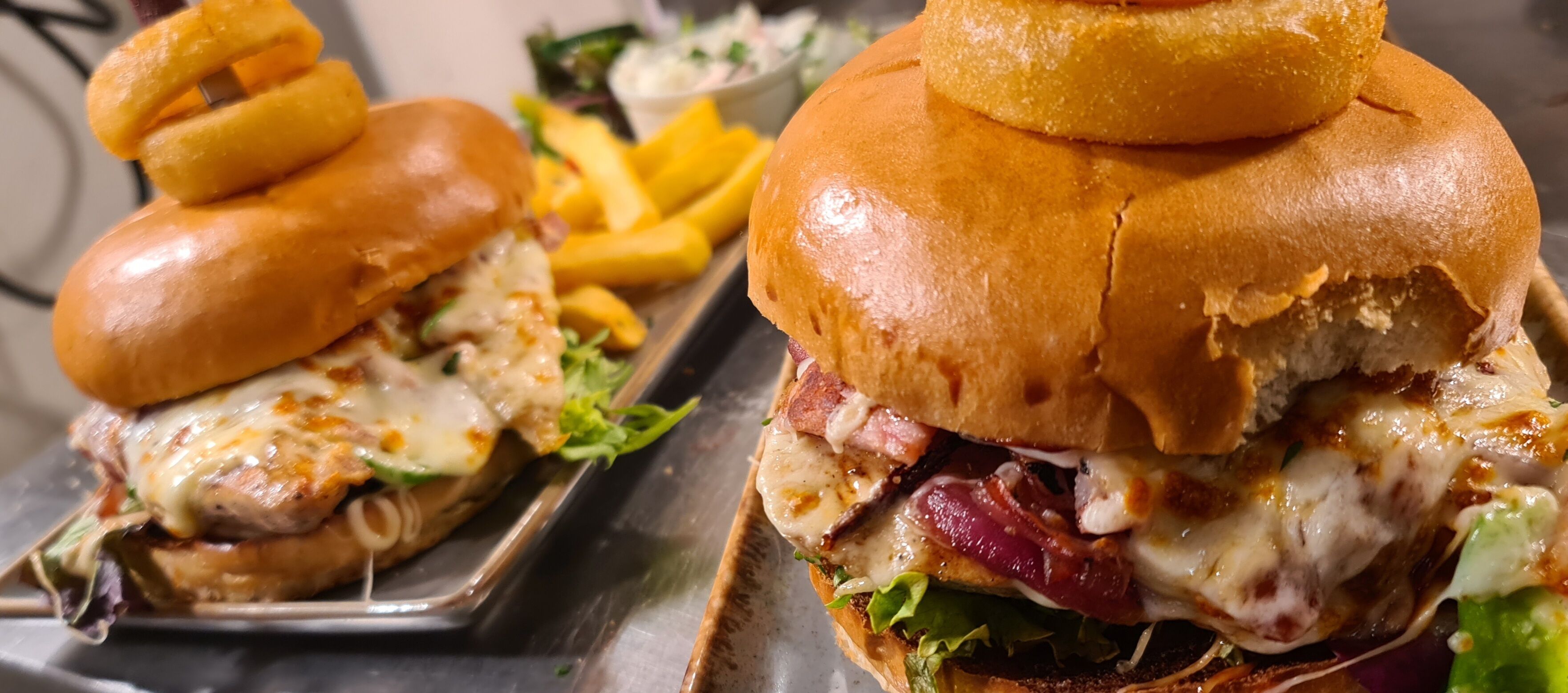 Primer plano de una hamburguesa con queso y lechuga, acompañada de papas fritas y una ensalada pequeña.