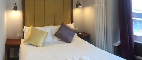 Una habitación de hotel con una cama grande, dos mesitas de noche, un cabecero y una ventana con cortinas.