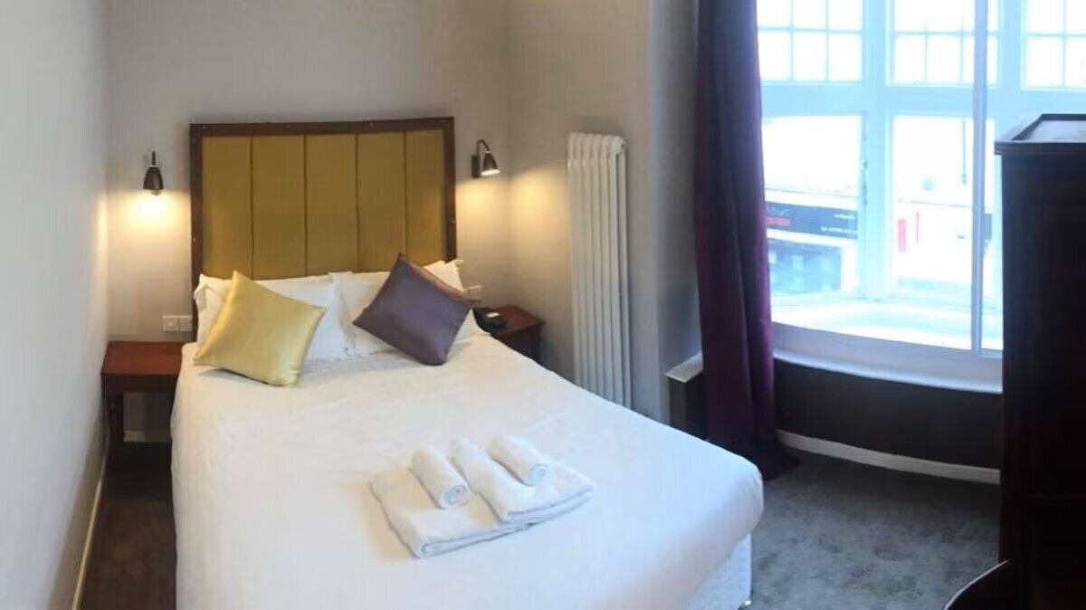 A hotel room with a large bed, two bedside tables, a window with curtains, and a radiator.
