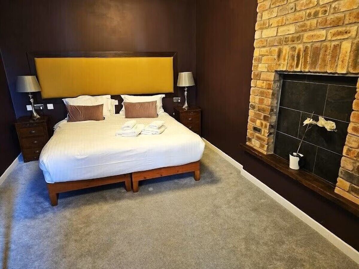 A bedroom with a large bed, a fireplace, and two bedside tables with lamps.