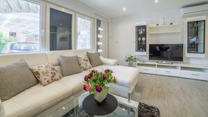 A modern living room with a beige sofa, a glass coffee table, and a TV on a white stand. - Apartments Milenka (Split)