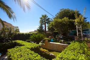 A well-maintained garden with various plants and a palm tree, a stone wall, and a swing set. - Apartments Milenka (Split)