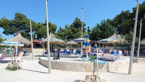 A beachside area with sun loungers, umbrellas, and a stone wall. - Apartments Milenka (Split)