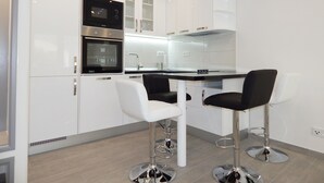 A modern kitchen with white cabinets, a black oven, a stainless steel sink, and two black bar stools. - Apartments Milenka (Split)
