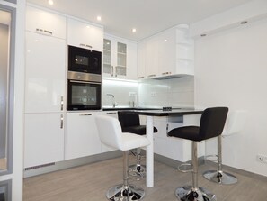 A modern kitchen with white cabinets, a black oven, a stainless steel sink, and two black bar stools.