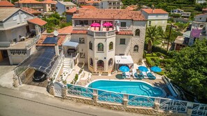 A villa with a swimming pool, a balcony with a red umbrella, and a view of the surrounding village and mountains. - Apartments Milenka (Split)