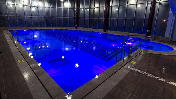 An indoor swimming pool with blue lighting, surrounded by a tiled floor and walls with a grid pattern. - Grand Hotel Terme (Kirsehir)