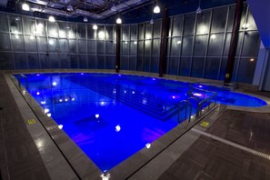 An indoor swimming pool with blue lighting, surrounded by a tiled floor and walls with a grid pattern. - Grand Hotel Terme (Kirsehir)