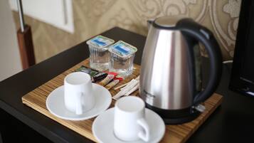 A breakfast tray with two white cups, a silver electric kettle, and two containers of yogurt on a wooden table.
