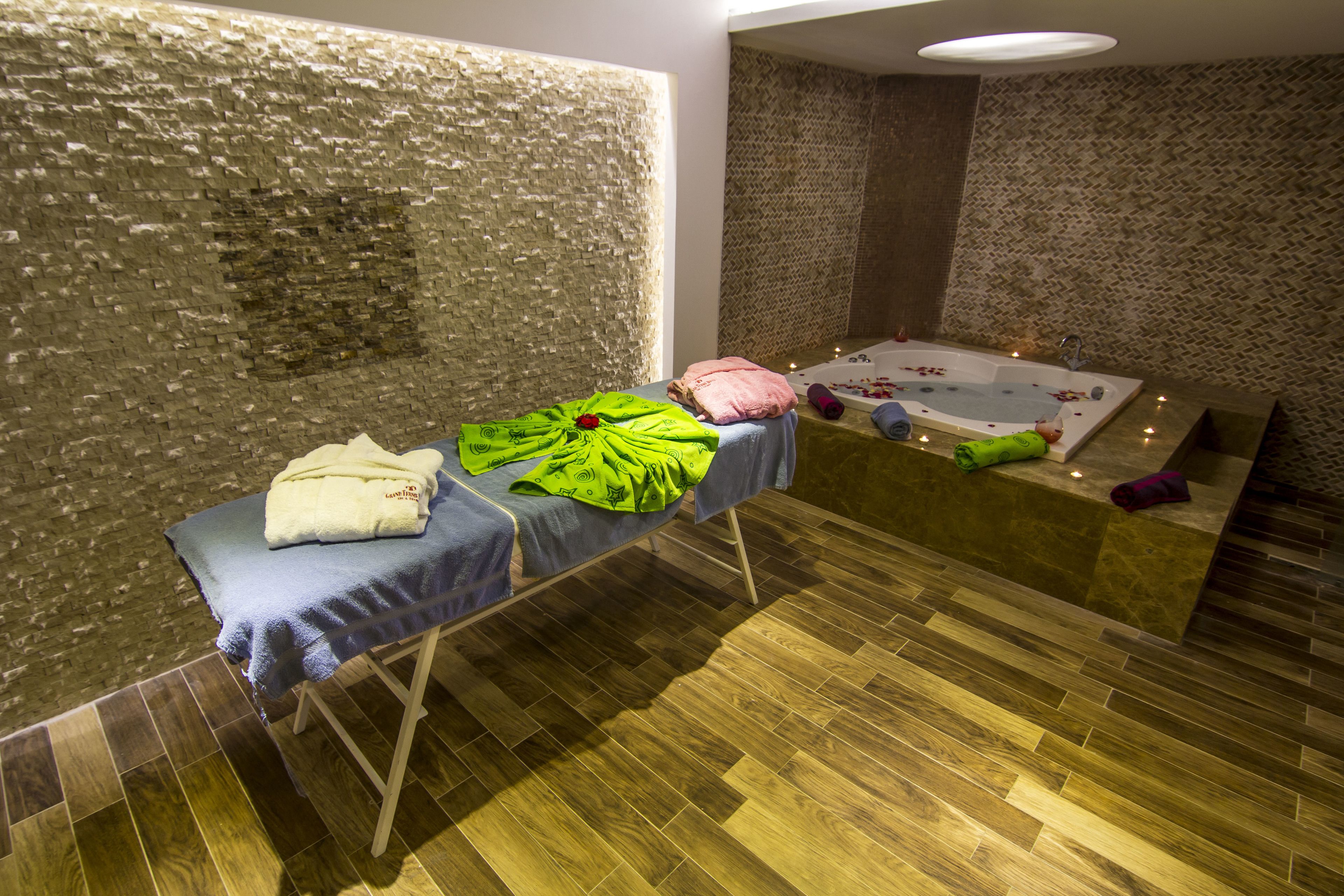 A spa room with a massage table, a bathtub, and wooden flooring.