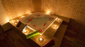 A spa area with a large bathtub surrounded by candles and rose petals. - Grand Hotel Terme (Kirsehir)