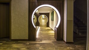 A hallway with a circular illuminated archway, wooden paneling, and a patterned floor. - Grand Hotel Terme (Kirsehir)