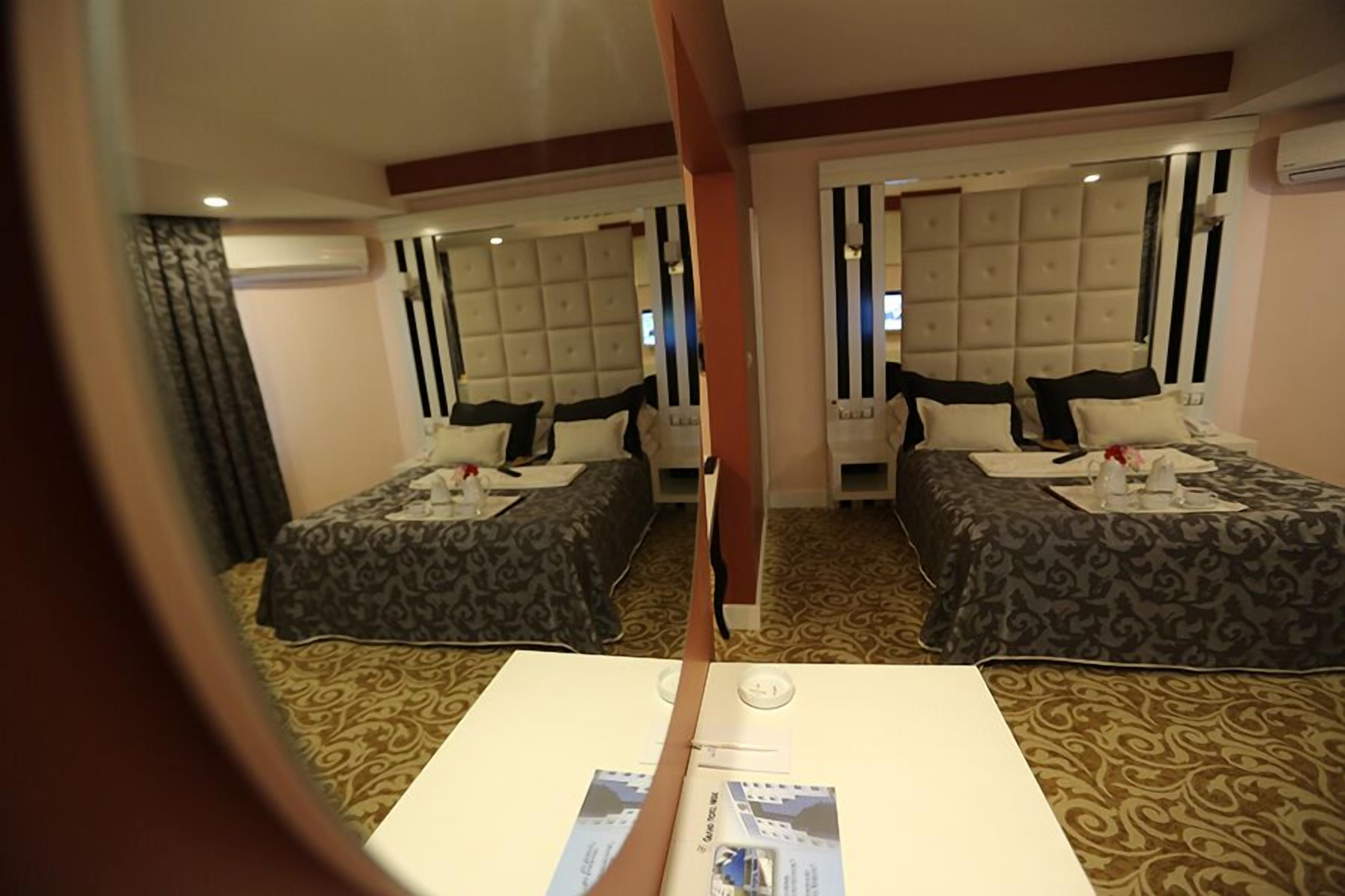 A hotel room with two beds, each with a tufted headboard, a small table with a tray, and a mirror above the bed.