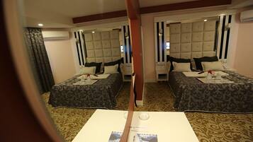 A hotel room with two beds, each with a tufted headboard, a small table with a tray, and a mirror above the bed.