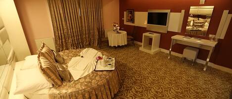 Una habitación de hotel con una cama grande, un escritorio, un televisor y un espejo.