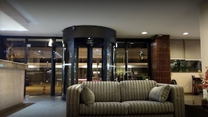 A lobby with a striped sofa, a glass elevator, and a modern interior design. - Niterói Palace Hotel (Niteroi)