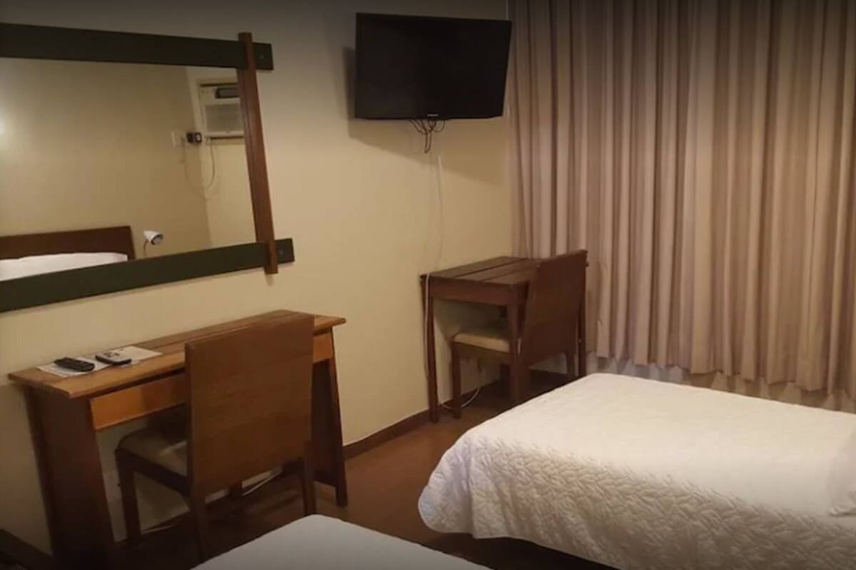 A hotel room with a bed, a desk, a chair, a television, and a window with curtains.
