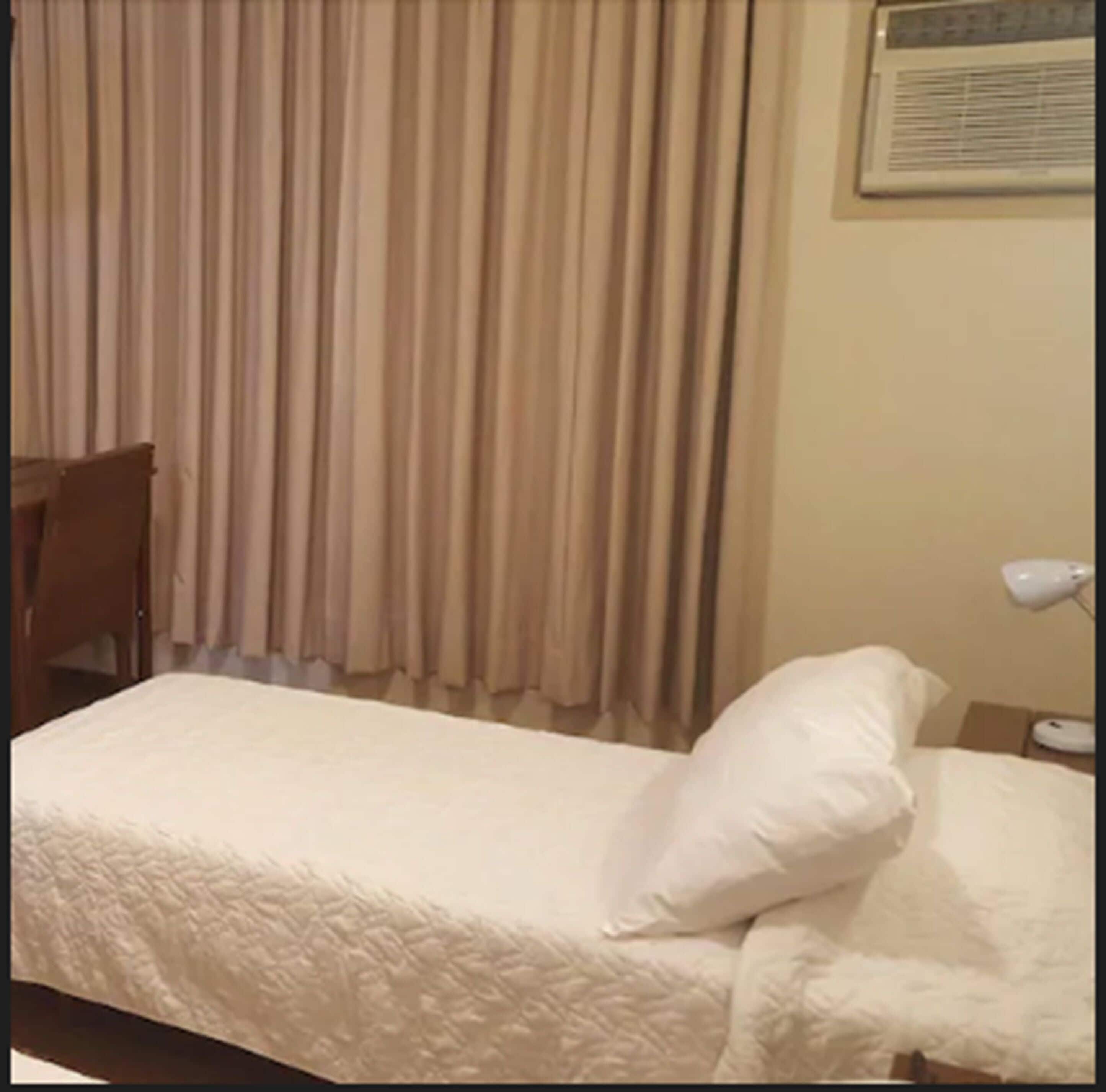A hotel room with a bed, a chair, a desk, a lamp, and a window with curtains.
