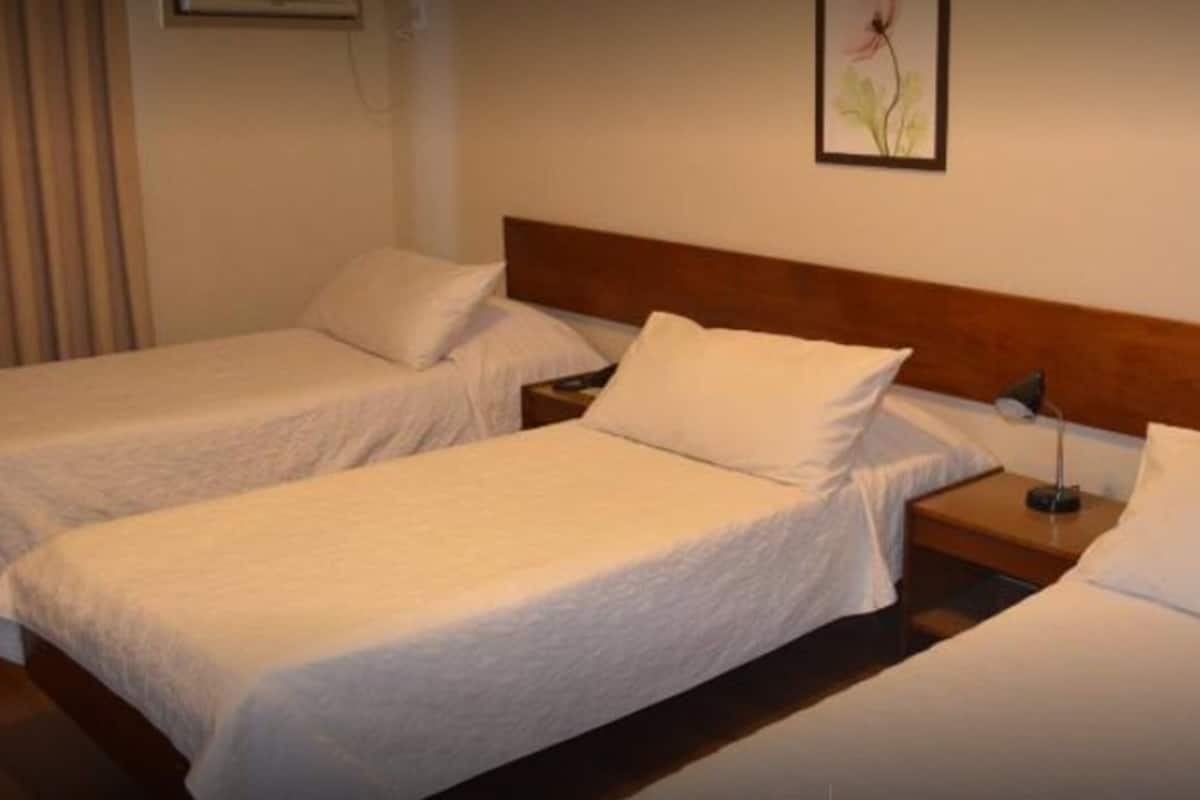 A hotel room with two single beds, a wooden headboard, a bedside table with a lamp, and a framed picture on the wall.