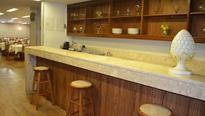 A bar area with wooden stools, a marble countertop, and shelves with glassware and plates. - Niterói Palace Hotel (Niteroi)