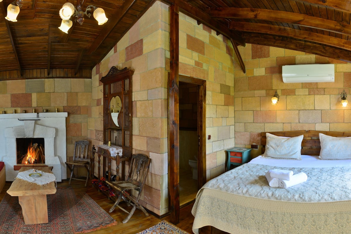Um quarto acolhedor com lareira, cama com toalhas bem dobradas e teto de madeira rústica.