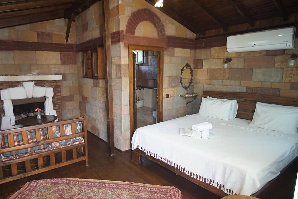 Um quarto com uma cama, um banco com estofamento floral, uma lareira e uma parede de pedra.