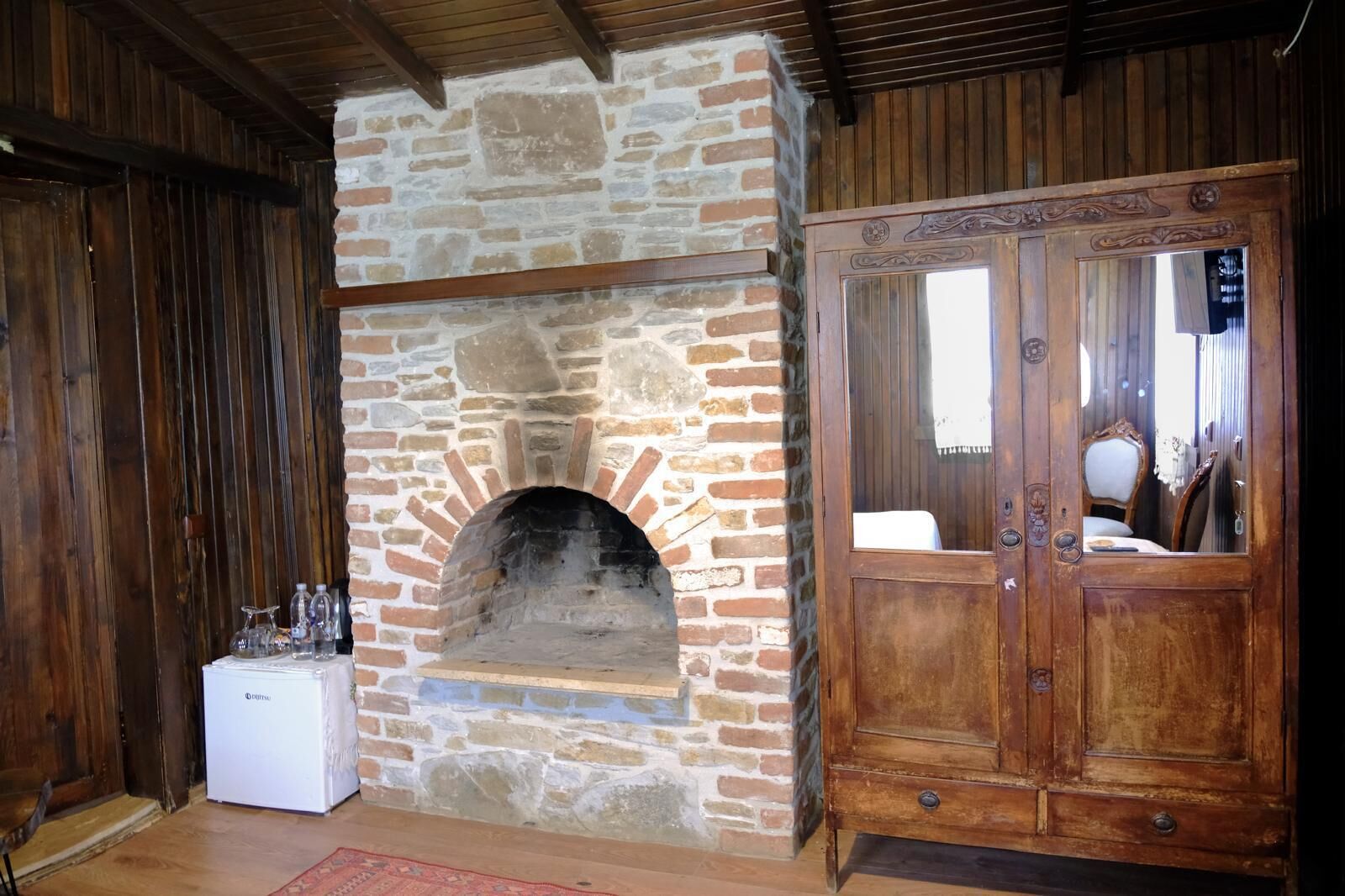 A stone fireplace with a white appliance next to it, a wooden cabinet with a mirror, and a wooden ceiling.