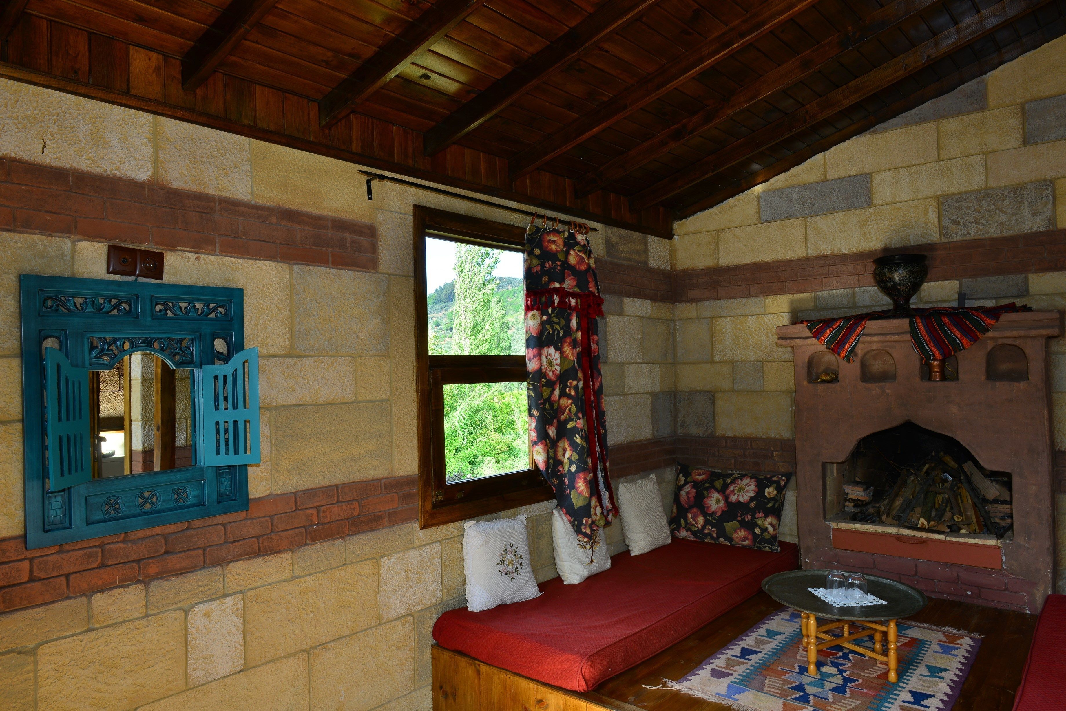 Una habitación acogedora con un banco de madera, una pequeña mesa, una chimenea y una ventana con cortinas.