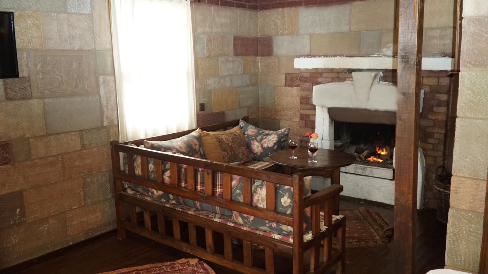 A cozy room with a wooden bench, a fireplace, and a stone wall.