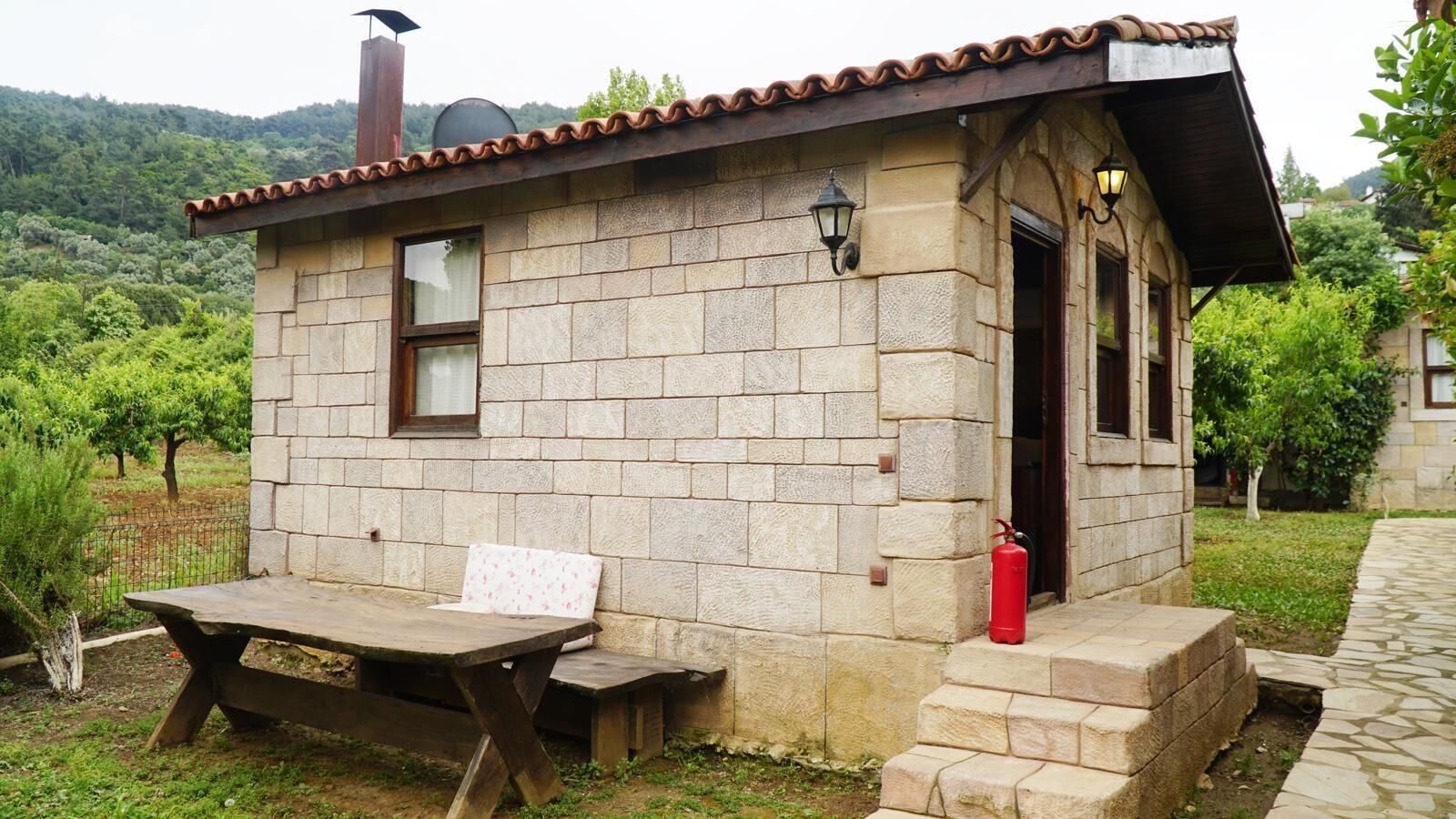 Una cabaña de piedra con banco y mesa de madera, un extintor y una chimenea.