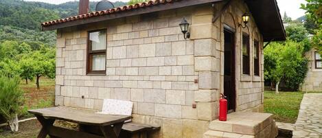 Una cabaña de piedra con banco y mesa de madera, un extintor y una chimenea.