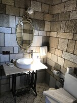 Un baño con pared de piedra, un lavamanos blanco, un espejo, un inodoro y un suelo estampado.