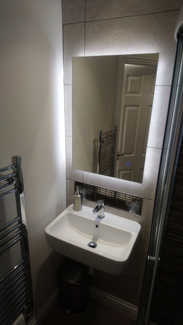 Une salle de bain avec un lavabo blanc, un miroir au-dessus et un porte-serviettes à gauche.