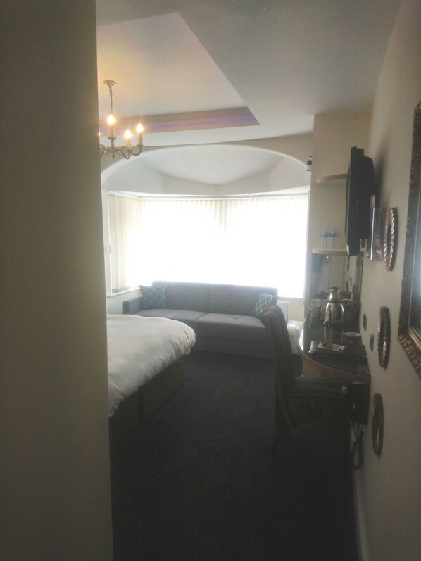 Une chambre d’hôtel avec un lit, un canapé, un bureau avec un téléphone et une fenêtre avec des rideaux.