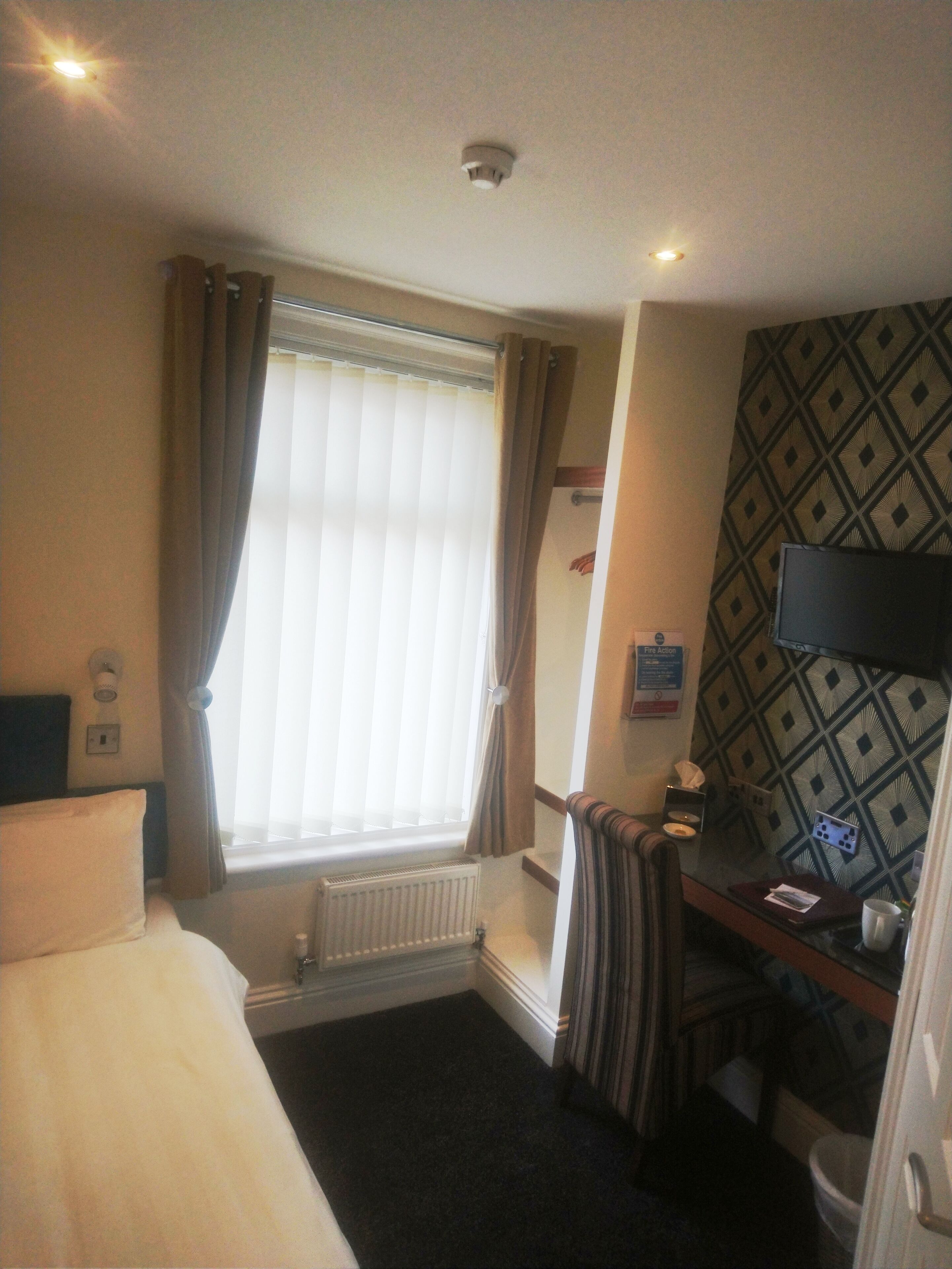 Habitación de hotel con cama, escritorio, radiador, ventana con cortinas y pared con diseño.