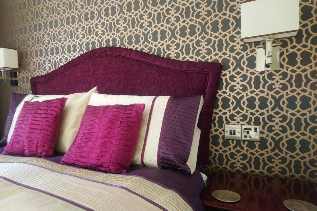 Una cama bien hecha con cabecera, una lámpara de pared y un enchufe.