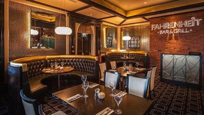 Et restaurantinteriør med en buet siddeplads i sort læder, borde med vinglas og en mur med navnet 'FAHRENHEIT BAR & GRILL'.