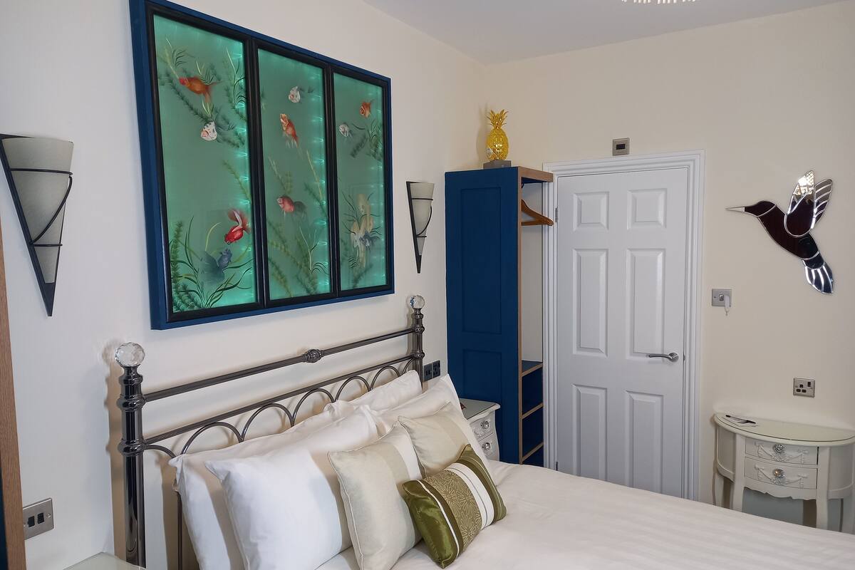 Un dormitorio con cama, mesita de noche, cómoda, estante en la pared y una puerta.