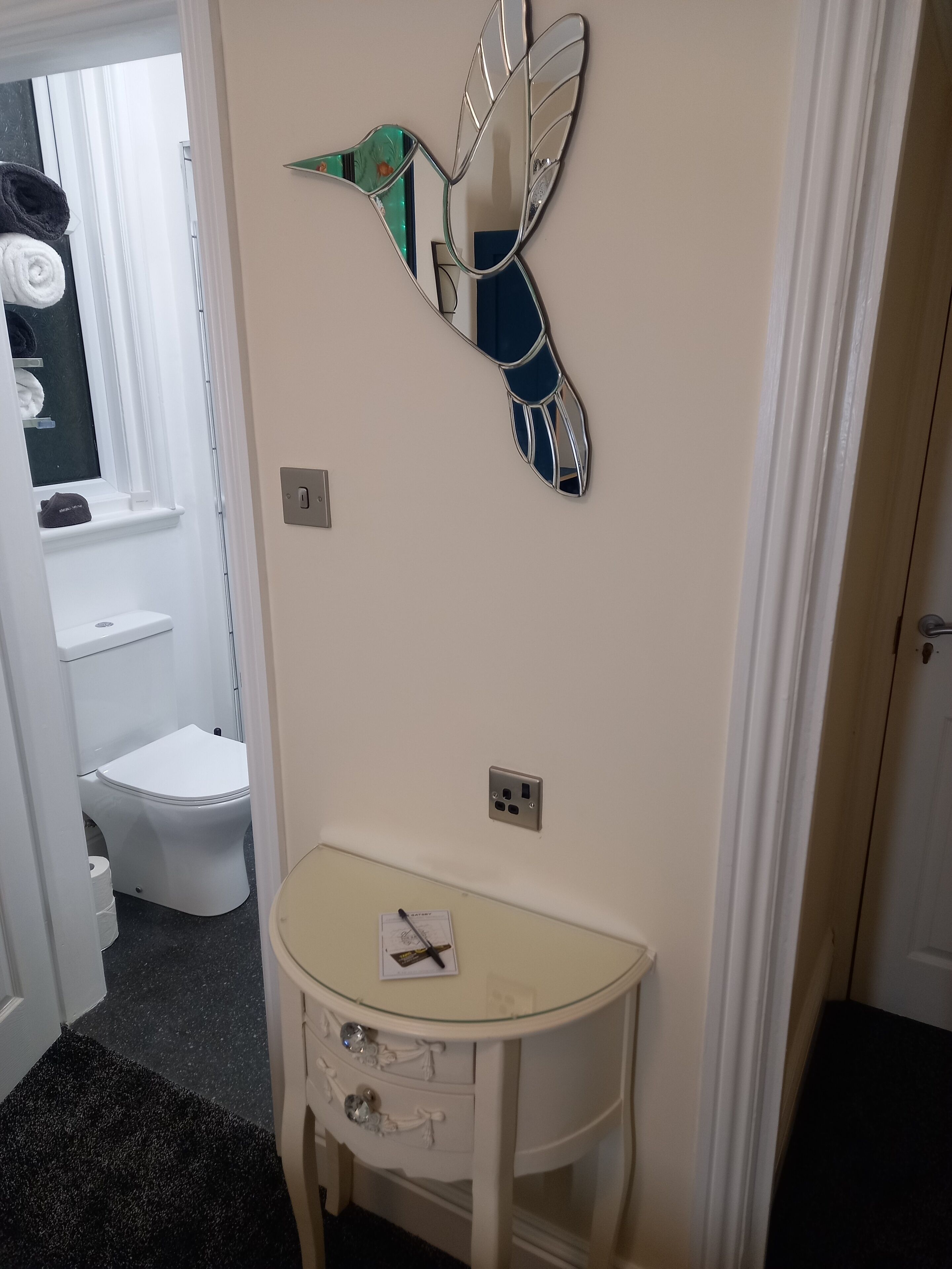 Een badkamer met een wit toilet, een glazen wastafel met een decoratieve spiegel en een handdoekrek met handdoeken.