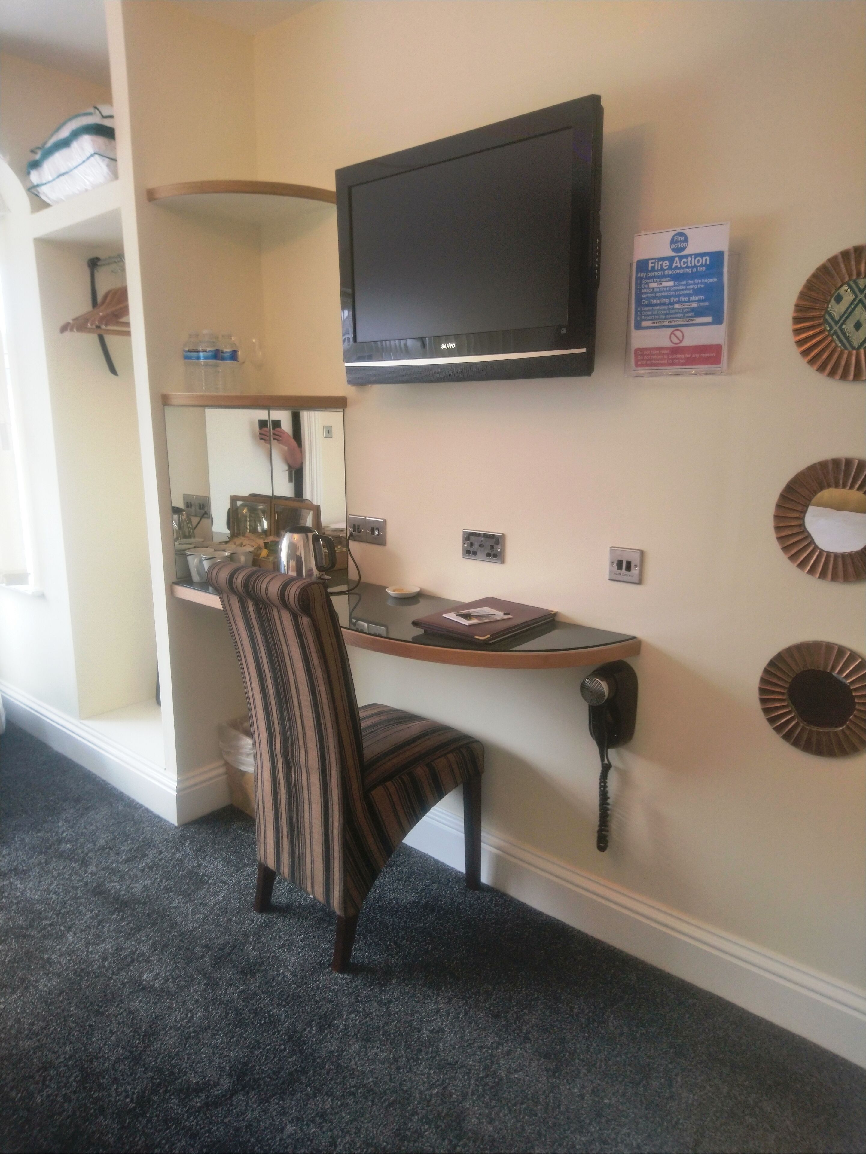 A small office space with a desk, chair, television, and a fire action sign.