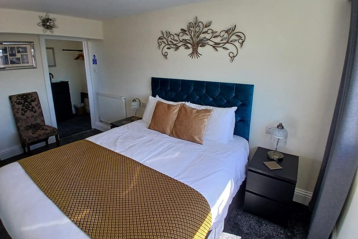 Una habitación de hotel con una cama grande, cabecera, mesita de noche y decoración en la pared.