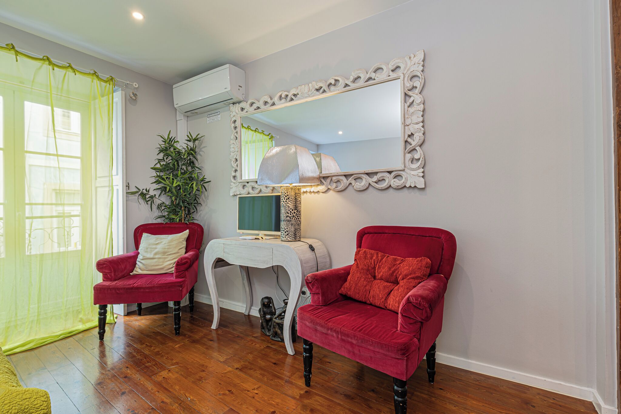 A room with two red armchairs, a white side table, a mirror, and a potted plant.