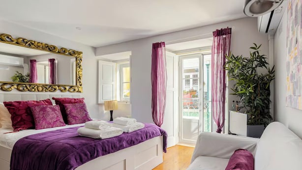 Une chambre à coucher avec un lit, un canapé blanc, un grand miroir et une fenêtre avec des rideaux.