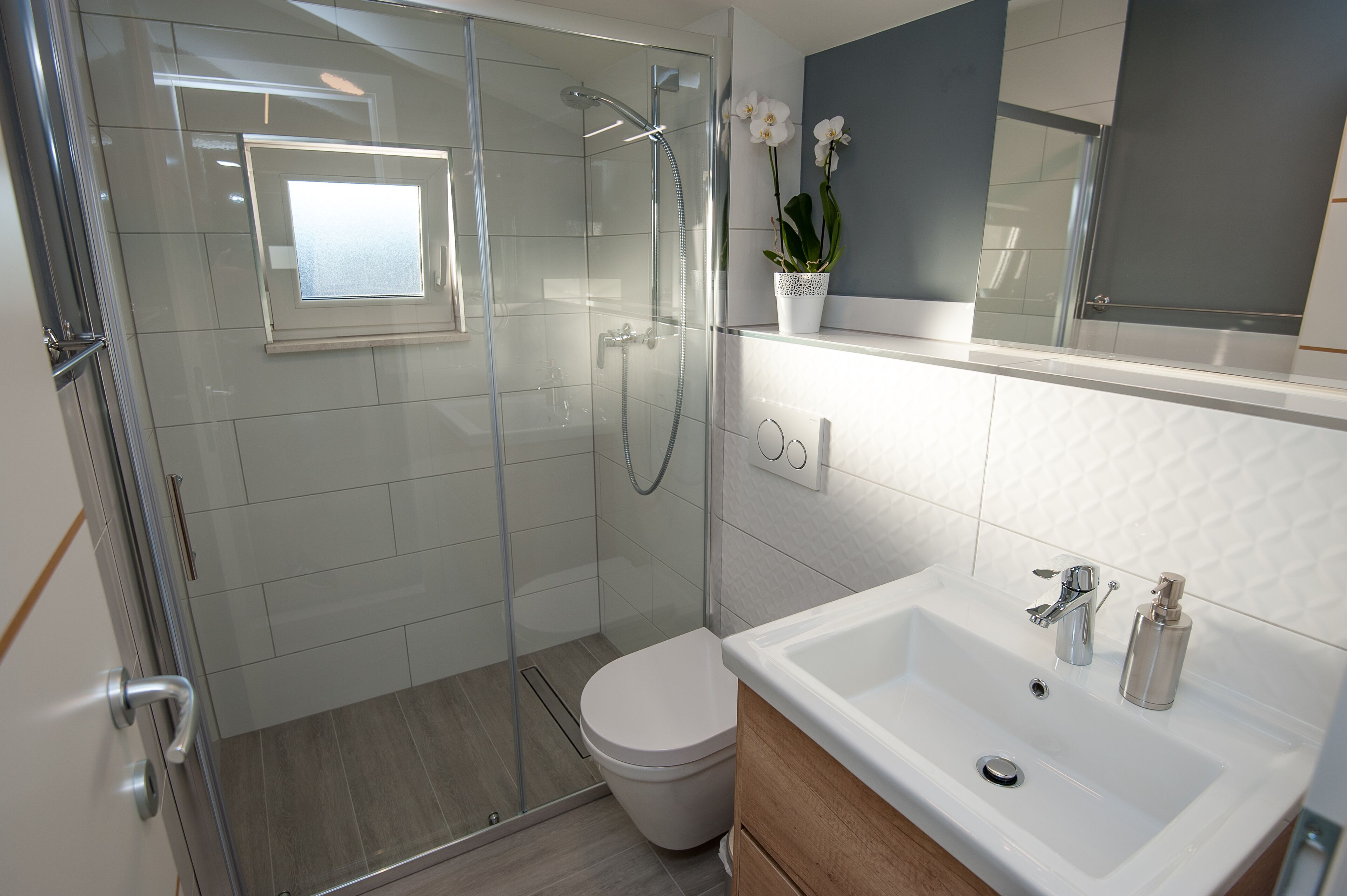 Ein modernes Badezimmer mit einer in Glas eingefassten Dusche, einer weißen Toilette und einem Waschbecken mit Spiegel darüber.