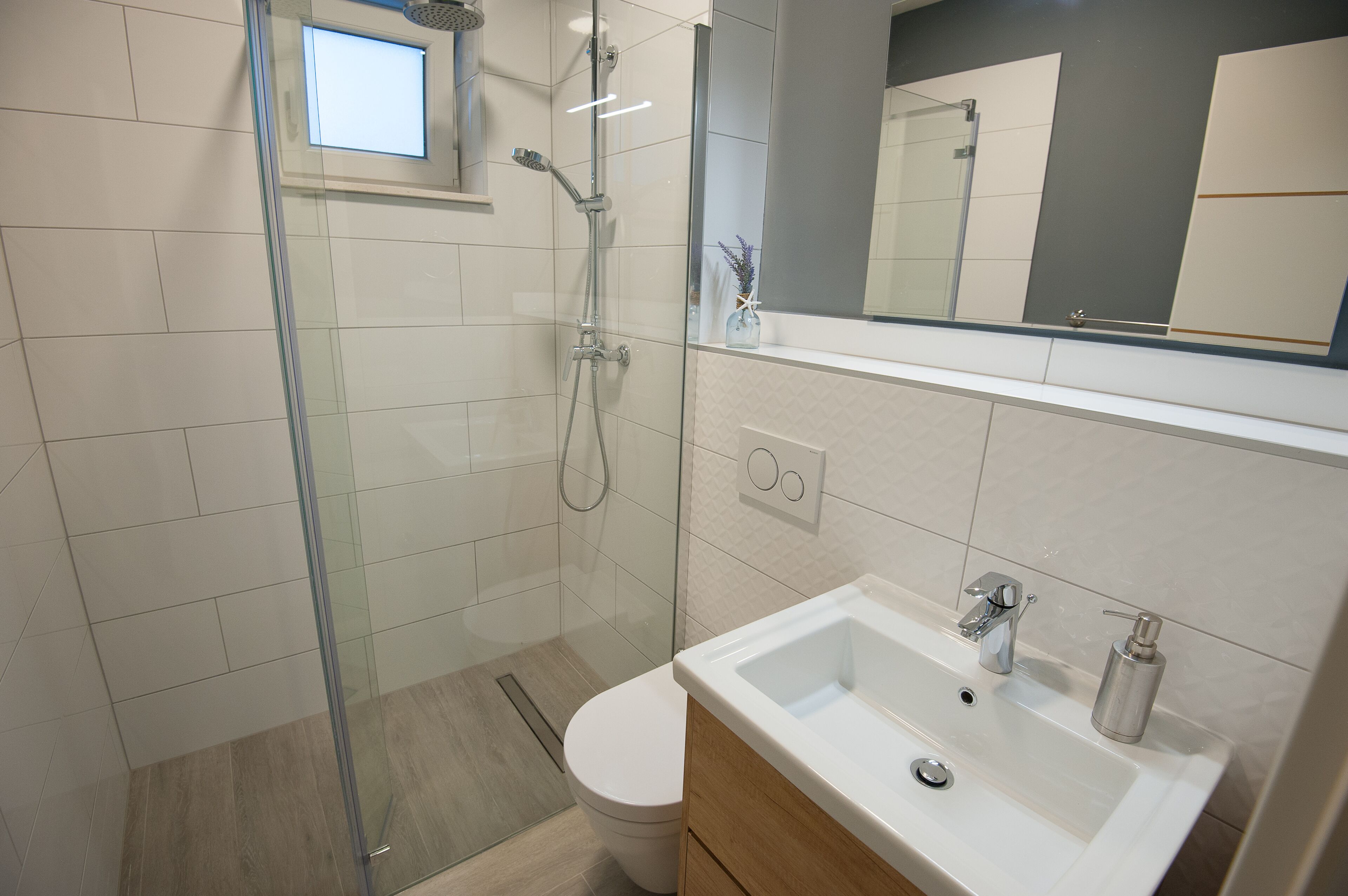 A modern bathroom with a glass-enclosed shower, a white sink with a soap dispenser, and a toilet.