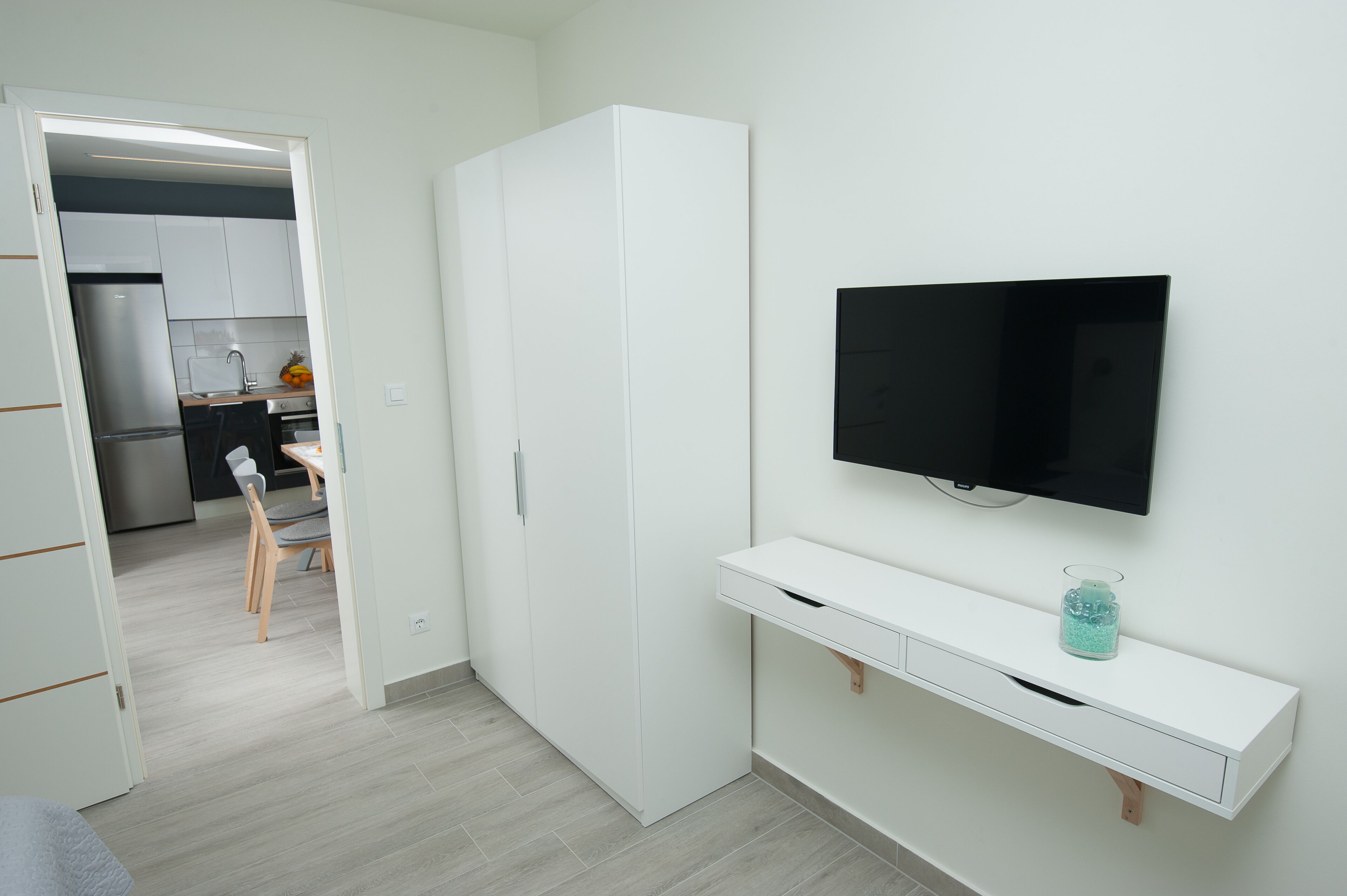 Una camera moderna con un armadio bianco, una TV a schermo piatto montata a parete e un tavolino con un vaso di vetro.