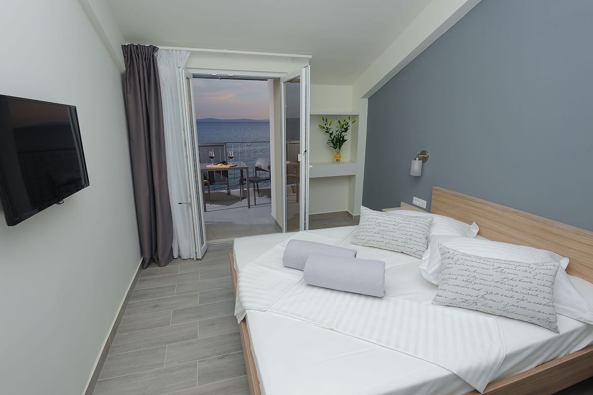 A hotel room with a bed, a TV, a balcony with a table and chairs, and a view of the sea.