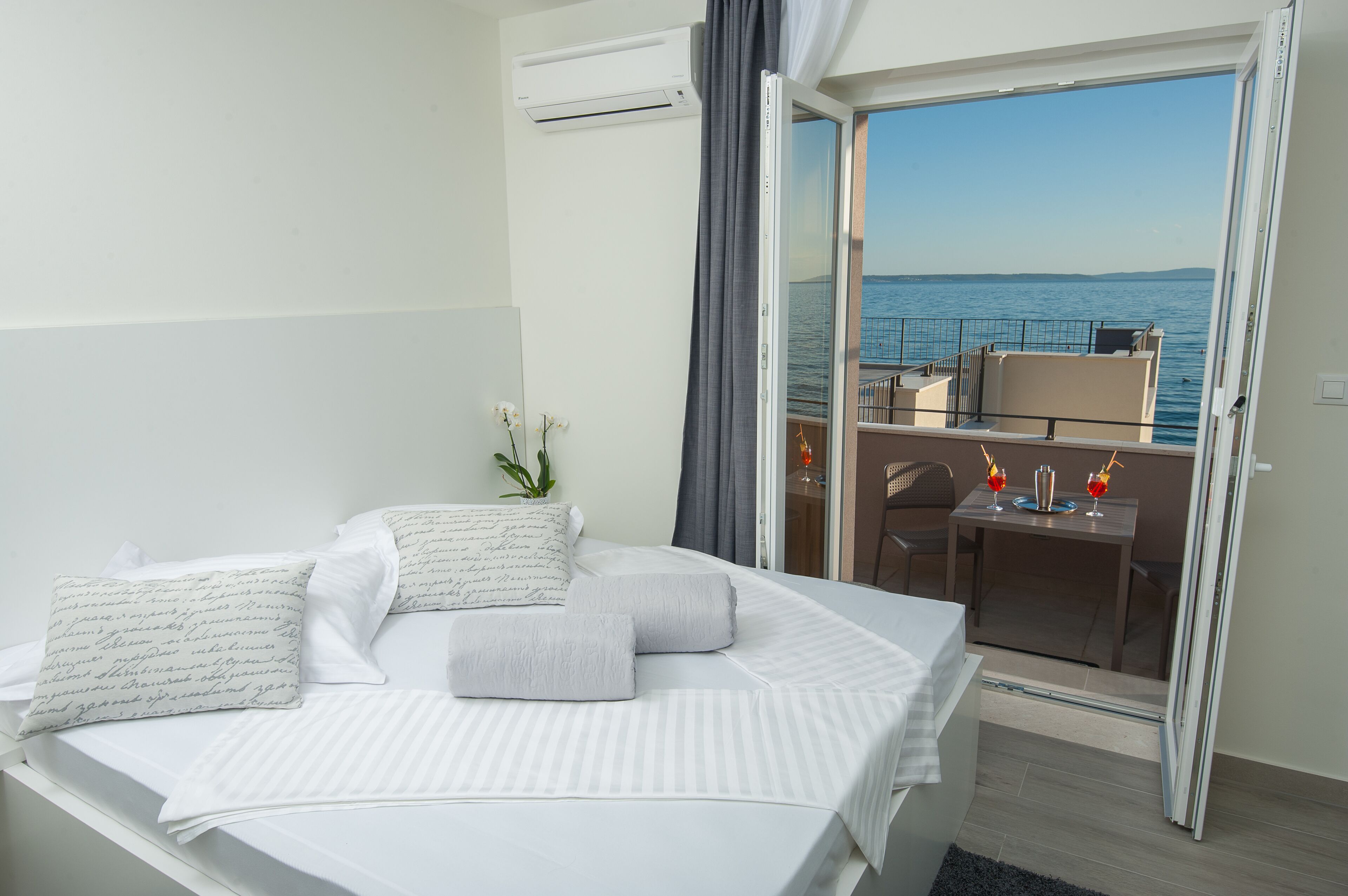 A hotel room with a bed, a small table with drinks, and a balcony with a view of the sea.